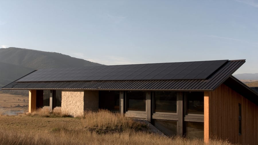 A long standing-seam roof carrying a flush, fully integrated array of matte-black modules, reading as one quiet surface